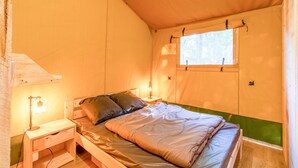 Una cama individual con estructura de madera, una mesita de noche con lámpara y una ventana que da a zonas verdes.