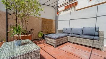 Eine überdachte Terrasse mit einem Rattan-Sofa, einem kleinen Tisch und Kübelpflanzen.