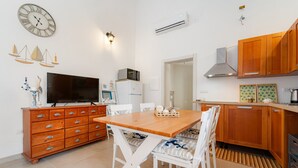 A modern kitchen with wooden cabinets, a dining table with chairs, a TV, and a refrigerator. - Holiday Home 'Sa Nue' with Private Terrace, Wi-Fi and Air Conditioning (Calasetta)
