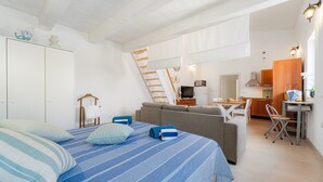 A bedroom with a bed, a sofa, a kitchen area, and a staircase. - Holiday Home 'Sa Nue' with Private Terrace, Wi-Fi and Air Conditioning (Calasetta)