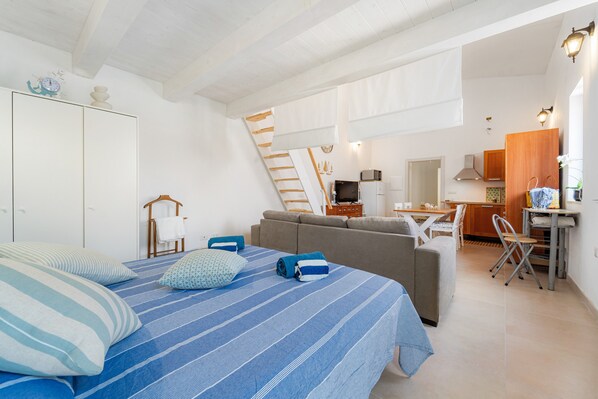 A bedroom with a bed, a sofa, a kitchen area, and a staircase.
