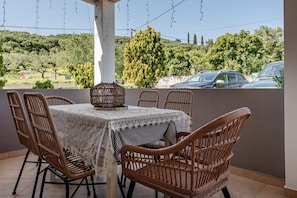 An outdoor patio with wicker chairs, a table with a lace tablecloth, and a decorative wicker centerpiece.