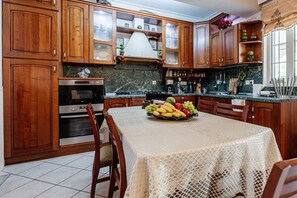 A kitchen with wooden cabinets, a dining table with a fruit bowl, and a coffee machine.