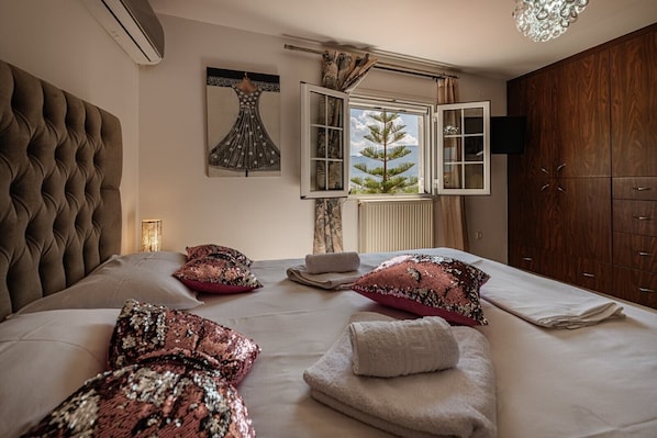 A bedroom with a tufted headboard, a large bed with decorative pillows, a window with a view of a tree, and a wooden wardrobe.