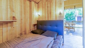 A wooden cabin bedroom with a bed, pillows, a headboard, and a view of an outdoor deck.