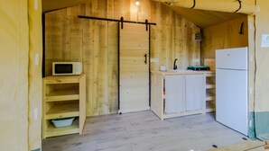 A compact kitchen with wooden walls, a microwave, a sink, and a refrigerator.