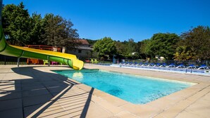 A swimming pool with a slide, surrounded by lounge chairs and trees.
