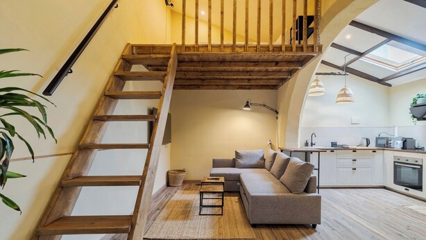 Ein modernes Loft mit einer Holztreppe, einem grauen Sofa und einer Küchenzeile.