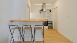 Une cuisine moderne avec un plan de travail en bois, trois tabourets de bar, un four encastré et une petite plante posée sur l’étagère.