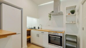 Une cuisine compacte avec des meubles blancs, un four encastré, une hotte en acier inoxydable et un plan de travail en bois.