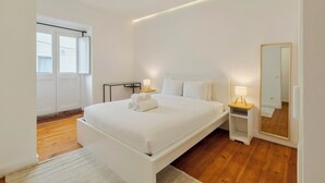 Une chambre moderne avec un grand lit, des tables de chevet avec des lampes, un miroir et une vue sur l’extérieur par une fenêtre.