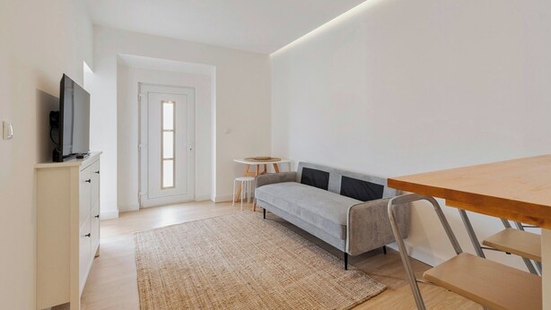 Un salon moderne et minimaliste, comprenant un canapé, un téléviseur, une petite table et une table à manger en bois.