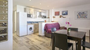 Een kleine keuken met een wasmachine, een eethoek met een tafel en stoelen, en een bank.