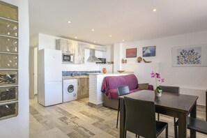 A compact kitchen with a washing machine, a dining area with a table and chairs, and a sofa.