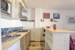 Une cuisine compacte équipée d’un évier, d’une cuisinière et d’un petit îlot central avec un pichet.