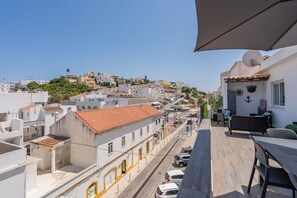 A balcony with a view of a city street, a dining area with outdoor furniture, and a satellite dish on the building. - Apartment 'Casa Terrace' with Private Terrace, Wi-Fi and Air Conditioning (Carvoeiro)