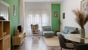 Uma sala de estar com sofá, mesa de jantar, televisão e estante de livros.