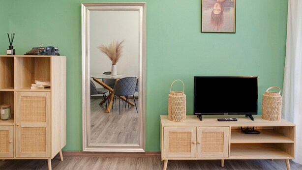 Quarto com um espelho grande, televisão, mesa de jantar com cadeiras e um armário com cestos de vime.