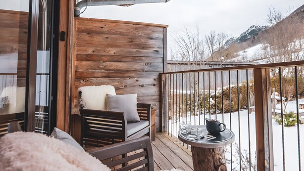 A wooden deck with a sofa and a chair, a table with a pitcher and glasses, and a view of a snowy landscape. - Le Fayard Loft – Character Apartment in Renovated Farmhouse, Hot Tub, Mountain Views (Aillon-le-Jeune)