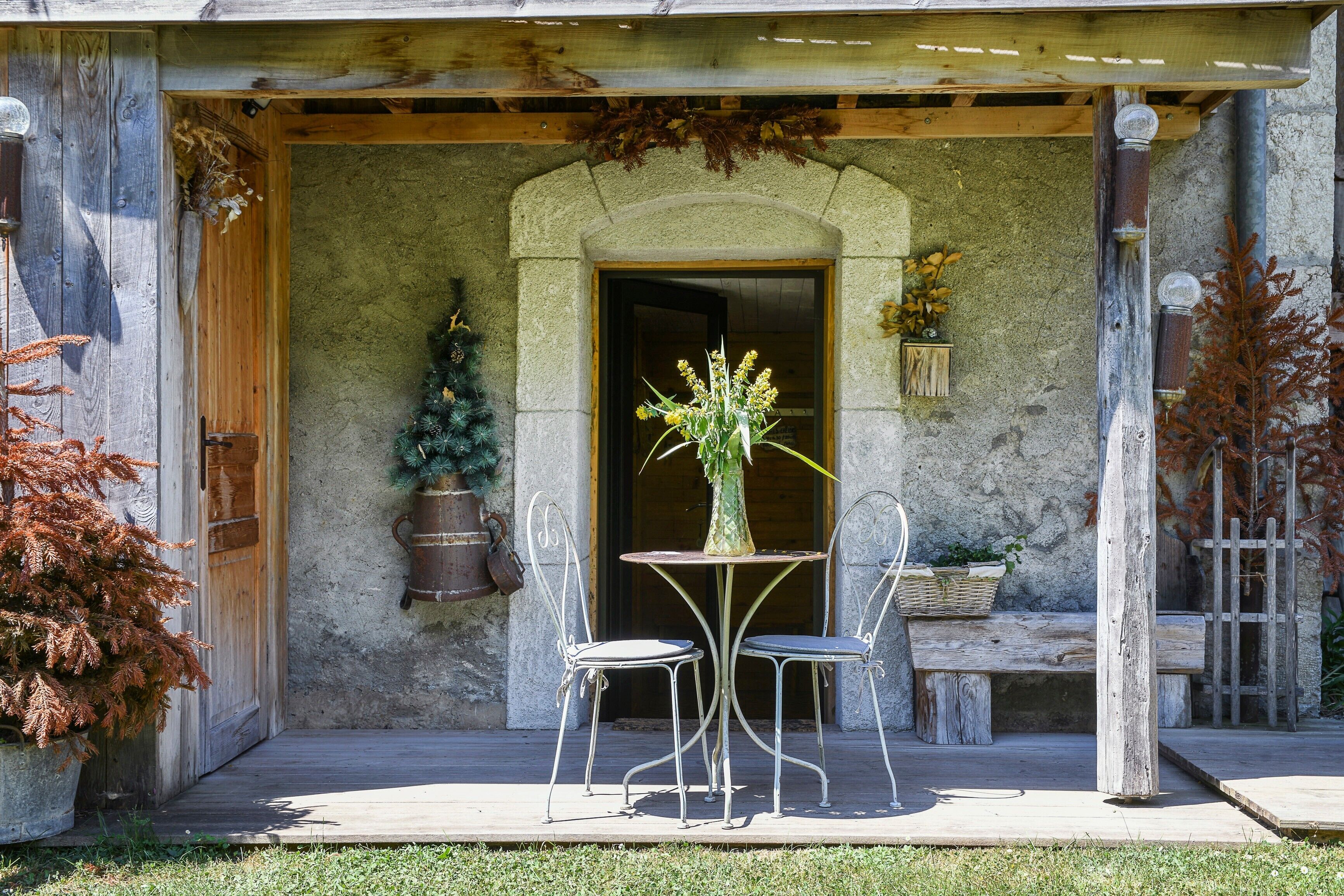 Ein rustikales Steinhaus mit einer Holztür, einer kleinen Veranda mit Tisch und Stühlen und einem Blumentopf.