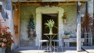 Ein rustikales Steinhaus mit einer Holztür, einer kleinen Veranda mit Tisch und Stühlen und einem Blumentopf.