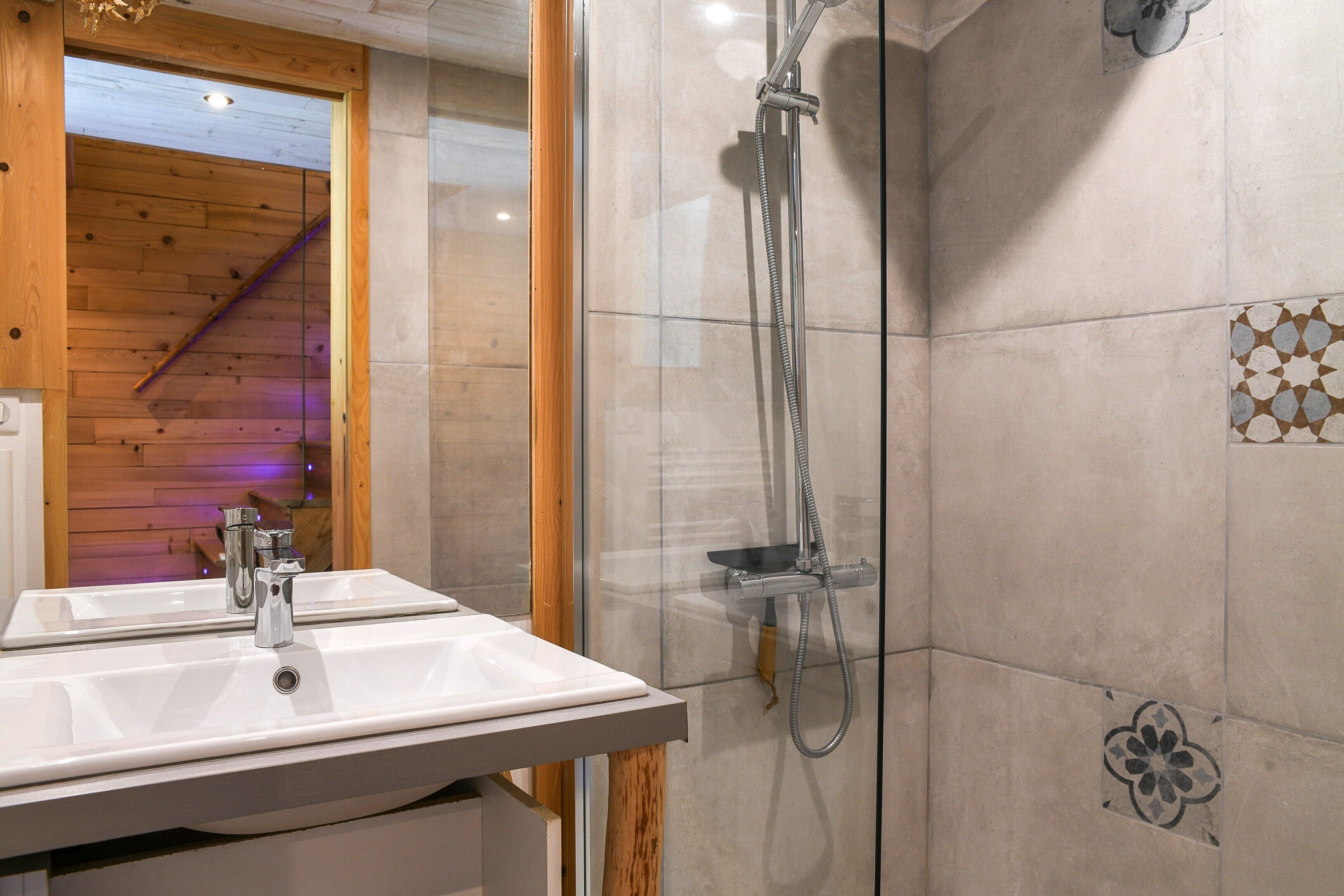 A bathroom with a white sink, a glass shower enclosure, and a wooden interior.