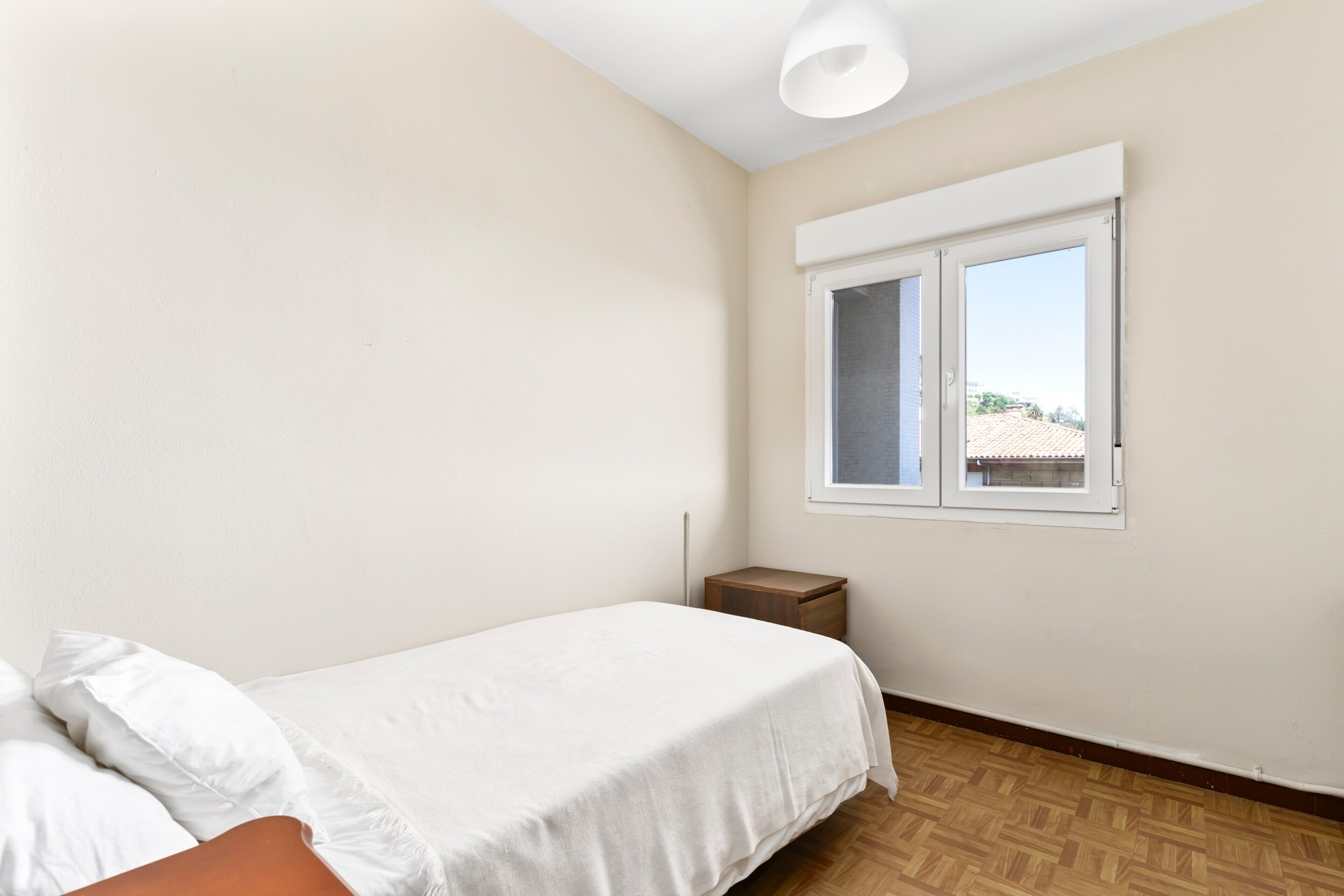 Ein Schlafzimmer mit Bett, Nachttisch, Fenster und Deckenleuchte.