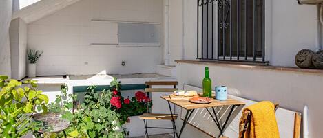 A small outdoor patio with a wooden table, chairs, a bottle, and a towel.