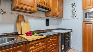 A kitchen with wooden cabinets, a stainless steel sink, a cutting board with vegetables, and a microwave. - Holiday Home 'El Fontanin, Tu Descanso Marinero' with Private Terrace (Lastres)
