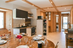 A wooden interior with a dining table set for four, a kitchen area with appliances, and a laundry room. - Ciméléon Haut Cottage – Authentic Mountain Charm, Mountain View, Terrace, Sleeps 6 (Aillon-le-Jeune)