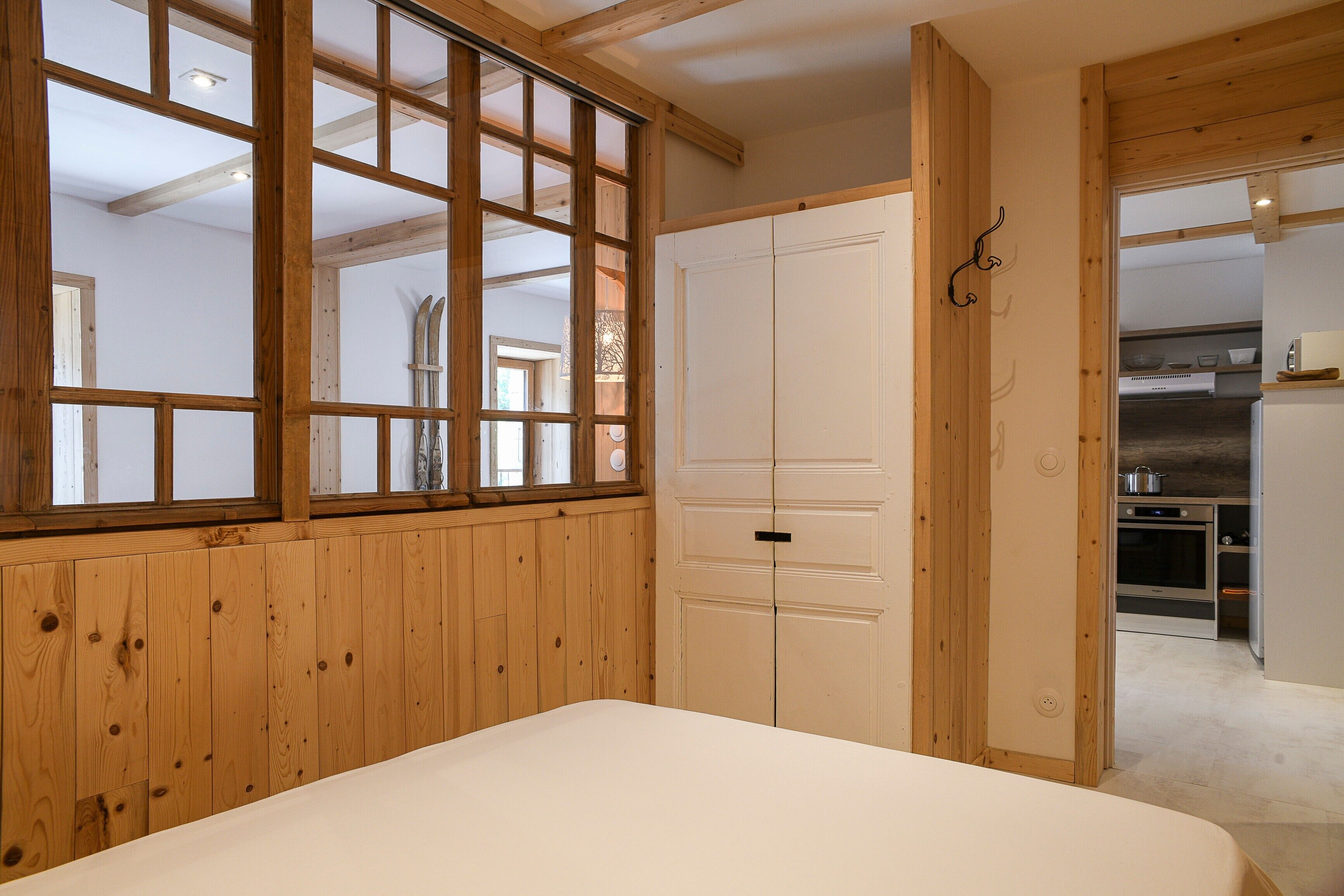 Un dormitorio con pared de paneles de madera, una cama, un armario y vistas a una zona de cocina.
