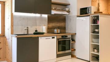 A compact kitchen with a dishwasher, oven, microwave, and wooden shelves.