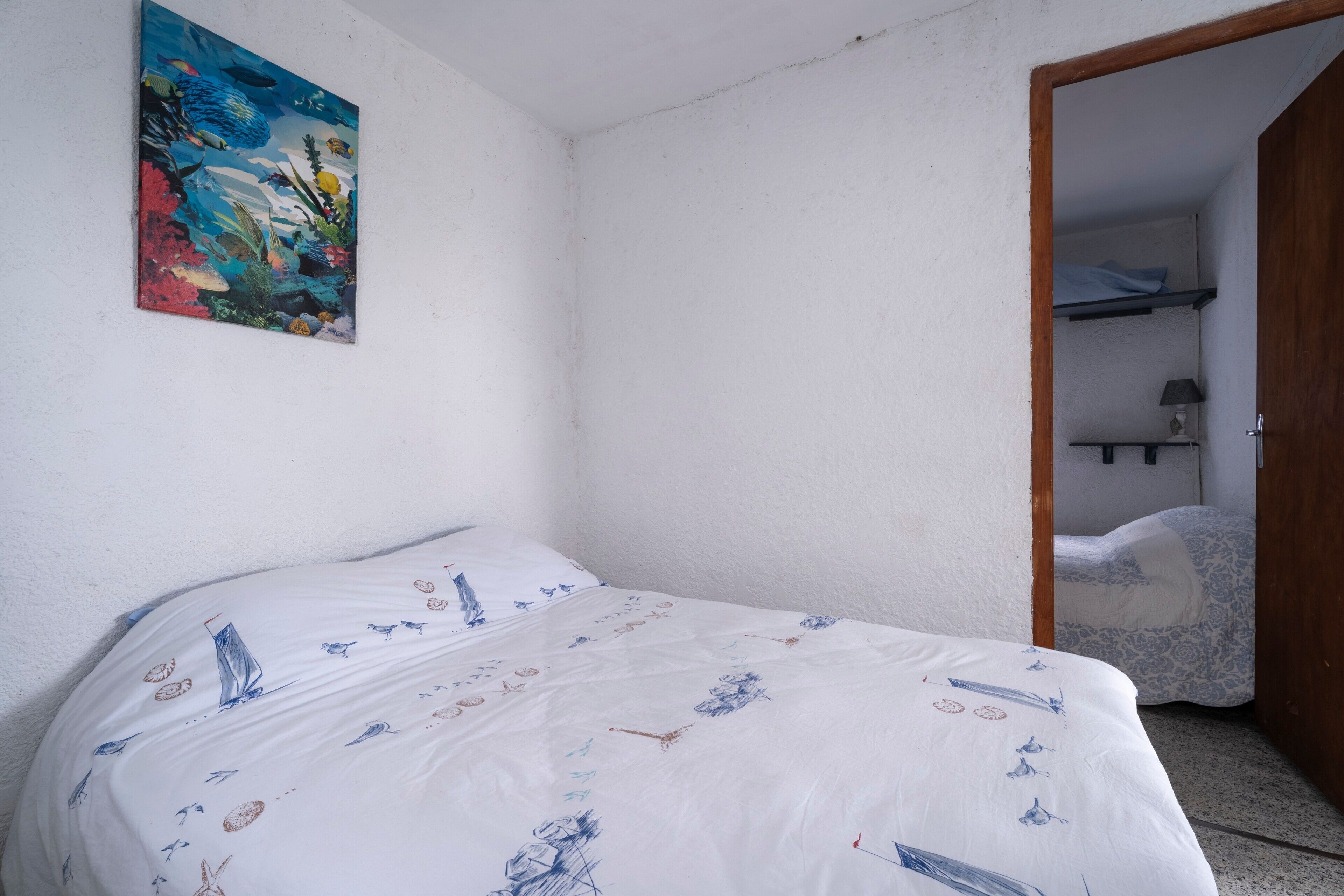 A bedroom with a bed, a painting, and a door leading to a bathroom.