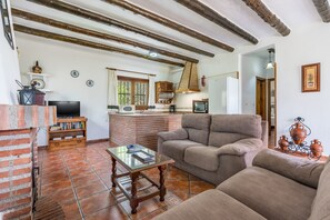 Ein Wohnzimmer mit Kamin aus Ziegelsteinen, einem Fernseher, einer Couch und einer Küchenzeile mit einer Pendelleuchte.