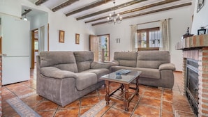 A living room with two sofas, a glass coffee table, exposed wooden beams, a fireplace, and a refrigerator.