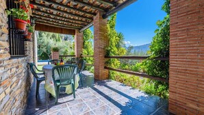 A covered patio with a table and chairs, a brick wall, and a view of greenery and mountains.