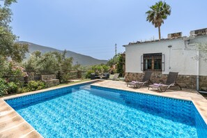 A swimming pool with lounge chairs and a stone wall, surrounded by greenery and a mountain view. - Holiday Home 'Las Gallinas Cottage' with Mountain View, Wi-Fi and Air Conditioning (Órgiva)