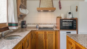 A kitchen with wooden cabinets, a built-in oven, a coffee maker, and a hanging fruit basket. - Holiday Home 'Benizarte' with Mountain View, Wi-Fi and Air Conditioning (Órgiva)