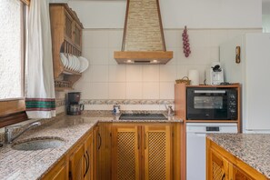 Una cocina con armarios de madera, horno empotrado, cafetera y una cesta de frutas colgante.