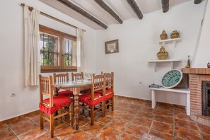 A dining area with a round table, wooden chairs, a window with curtains, and a brick fireplace.