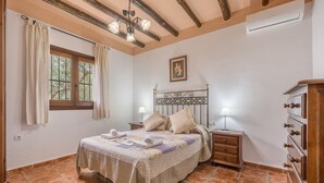 A bedroom with a bed, nightstands, a dresser, a window with curtains, a chandelier, and a wall-mounted air conditioner. - Holiday Home 'Benizarte' with Mountain View, Wi-Fi and Air Conditioning (Órgiva)