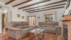 A living room with two sofas, a glass coffee table, exposed wooden beams, a fireplace, and a view of the outdoors. - Holiday Home 'Benizarte' with Mountain View, Wi-Fi and Air Conditioning (Órgiva)
