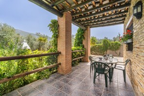 A covered patio with a brick column, a table with chairs, and a view of greenery and a mountain.