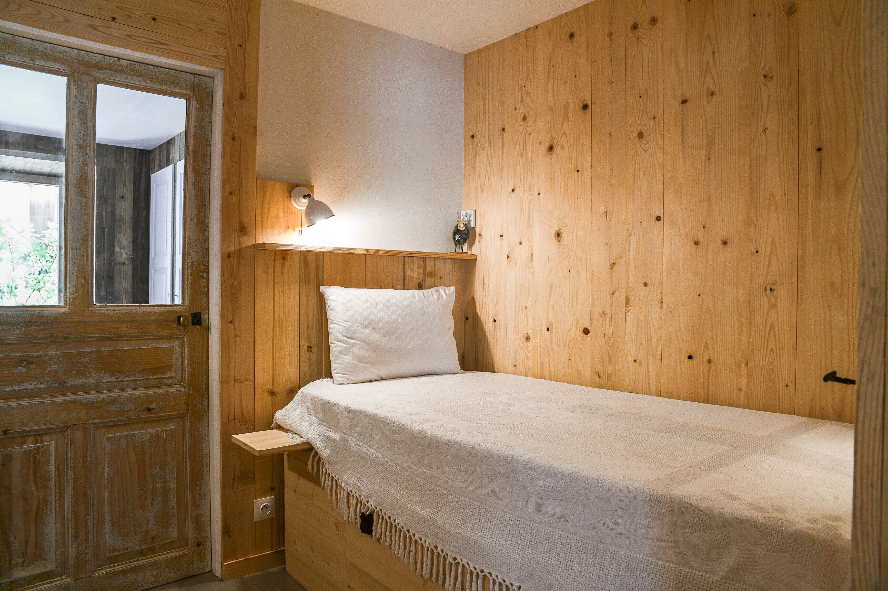 A wooden room with a bed, a nightstand, a lamp, and a door.