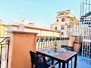 A rooftop terrace with a table and chairs, a potted plant, and a view of the cityscape.