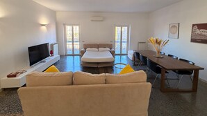 A modern hotel room with a sofa, a bed, a TV, a dining table, and two doors leading to a balcony. - Apartment 'Monti View' with Private Terrace, Wi-Fi and Air Conditioning (Roma)
