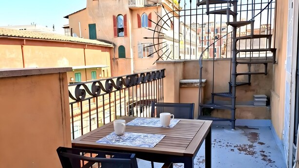 A balcony with a table and chairs, a spiral staircase, and a building with balconies in the background. - Apartment 'Monti View' with Private Terrace, Wi-Fi and Air Conditioning (Roma)