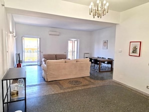 Amplia sala de estar con sofá, mesa de comedor y lámpara de araña.