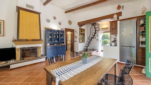 A spacious living area with a fireplace, a dining table, and a kitchen with a refrigerator and cabinets.