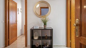 Een gang met een houten deur, een zwarte console tafel met spiegel, een potplant, een vogelkooi, een scheepsmodel en een bordje met de tekst 'SUITE CAVA'.